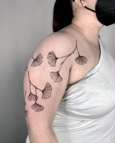 a woman with a mask on her face wearing a black and grey tattoo design that has ging sprouts growing out of it