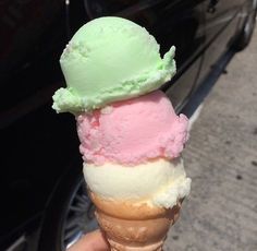 a hand holding an ice cream cone with pink, green and white flavors on it