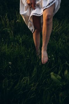 a woman standing in the grass with her legs crossed and wearing a white dress on