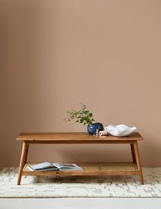 a wooden table with two vases and a book on it in front of a pink wall