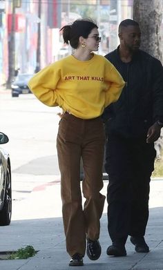 a man and woman walking down the street with one wearing a yellow shirt that says art that kill