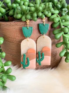 a pair of cactus shaped earrings sitting on top of a potted plant