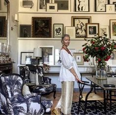 a woman standing in a living room next to a table with chairs and pictures on the wall