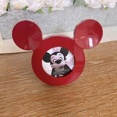 a red mickey mouse coaster sitting on top of a wooden table next to white flowers