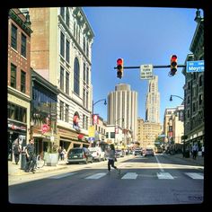 a man is crossing the street in front of some buildings and traffic lights on a sunny day