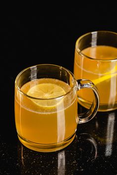 two mugs filled with lemon tea sit on a black countertop next to each other