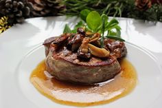 a steak covered in mushrooms and sauce on a white plate with green leafy garnish