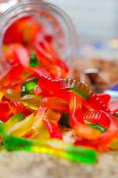 colorful gummy bears are spilling out of a glass jar on the ground next to other candies