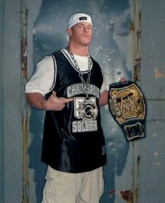 a man holding a wrestling belt and giving the thumbs up sign while standing in front of a wall