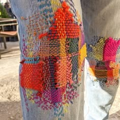 a person standing next to a bench wearing jeans with colorful designs on them and their legs