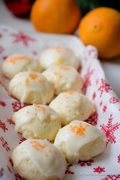 oranges and white frosted pastries are on a red and white napkin next to some oranges