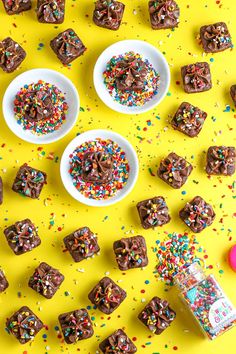 chocolate squares with sprinkles in small white bowls on a yellow surface surrounded by confetti