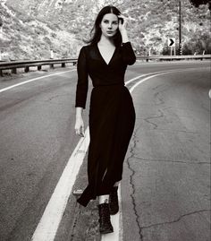 a black and white photo of a woman in a long dress on the side of a road