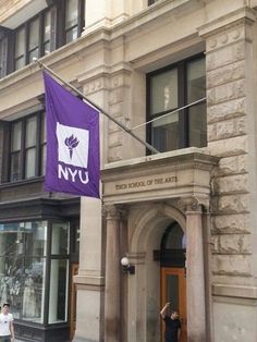 two people walking in front of a building with a purple flag hanging from it's side