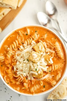 a bowl of pasta soup with bread and parmesan cheese on the side, ready to be eaten