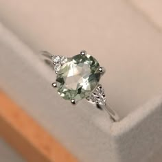 an engagement ring with a green stone surrounded by three diamond accents in a white box