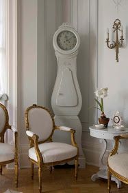 a white clock sitting on the side of a wall next to two chairs