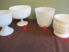 four white vases sitting next to each other on top of a brown tablecloth