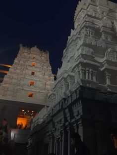 people are standing in front of an ornate white building at night with lights shining on it