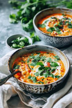 Two bowls of creamy soup garnished with cilantro, with small bowls of additional cilantro on the side. Green Coconut