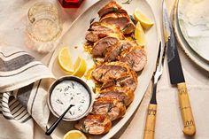 a white plate topped with meat and lemons next to a knife and fork on top of a table