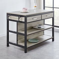 a kitchen island with two drawers and plates on the bottom shelf, in front of a window