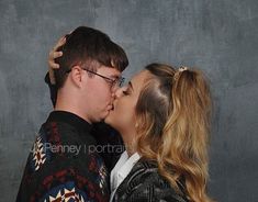 a man and woman kissing each other in front of a gray background