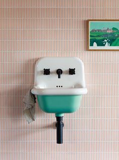 a bathroom sink with two faucets mounted to the wall next to a painting