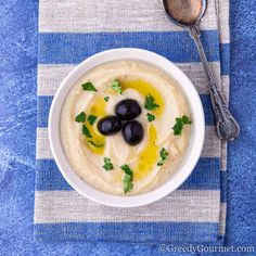 a bowl of hummus with olives and cilantro on a blue towel