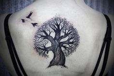 a woman's back with a tree tattoo on her shoulder and two birds flying around it