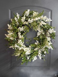 a wreath with white flowers and greenery hanging on the wall in front of a door