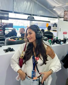 a woman wearing headphones standing in front of a booth at an electronics show with other people