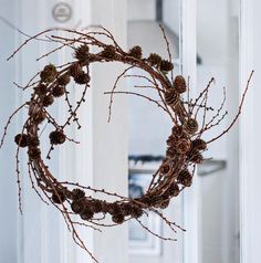 a wreath made out of pine cones hanging from the side of a white door with a mirror in the background