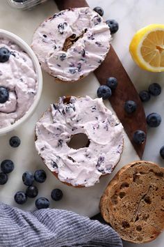 two bagels with frosting and blueberries on a cutting board next to sliced lemons