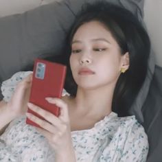 a woman laying down holding a red cell phone in her hand and looking at it