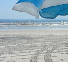 an umbrella is on the beach by the water's edge with tracks in the sand