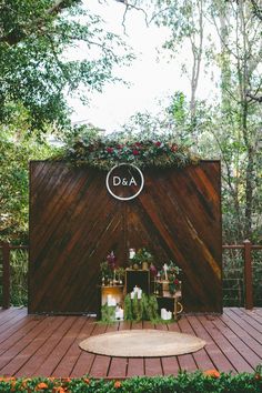 an outdoor ceremony setup with flowers and greenery on the back wall, surrounded by wooden planks