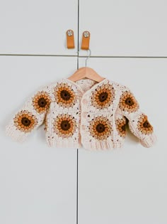 a crocheted sweater with sunflowers is hanging on a hook in front of a white wall