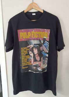 a black t - shirt with the words pulp fiction on it hanging from a wooden hanger