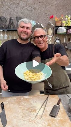 two men standing next to each other in front of a table with food on it