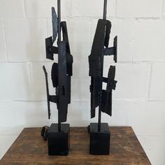 two black metal sculptures sitting on top of a wooden table next to a white brick wall