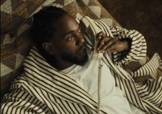 a man laying on top of a couch talking on a cell phone while wearing a striped jacket