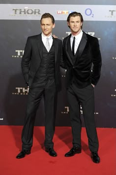 two men in suits standing on a red carpet