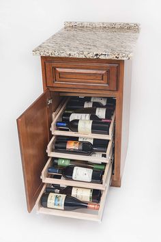 an open cabinet with several bottles of wine in the bottom drawer and marble counter top