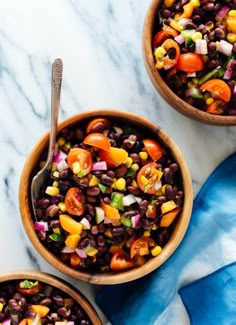 two wooden bowls filled with black beans and veggies next to a blue towel