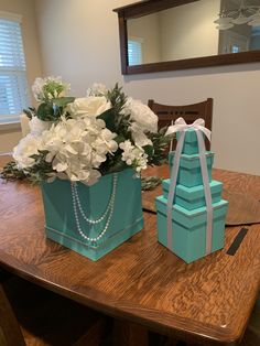 a blue box with flowers and pearls sits on a table next to a turquoise gift bag