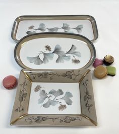 two plates with flowers and leaves painted on them next to some candies in front of them