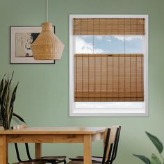 a dining room with green walls and wooden blinds on the windowsill, along with a bamboo table and chairs