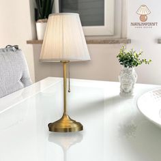 a white table with a lamp on it and a vase full of flowers next to it