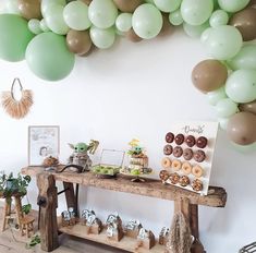 a table topped with donuts next to a wall filled with green and gold balloons